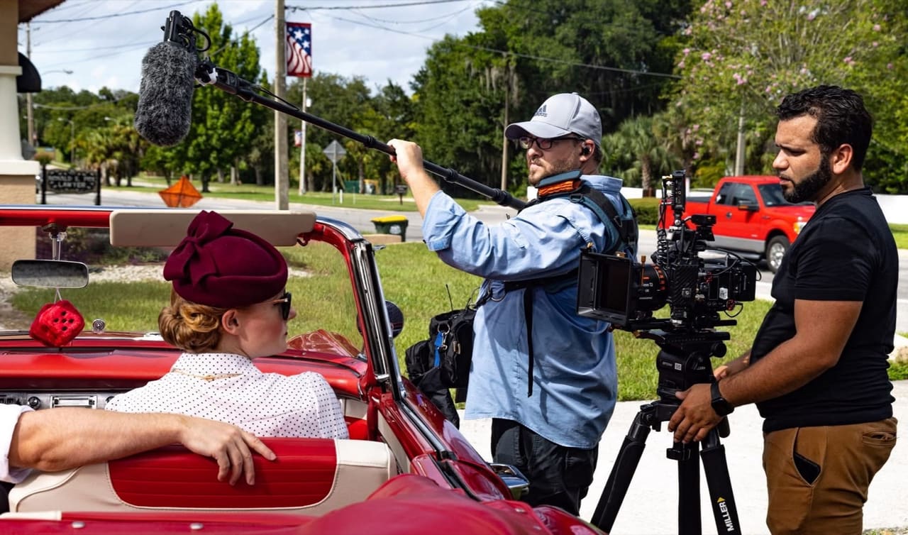 Boom operator and camera crew filming a scene in a classic red convertible