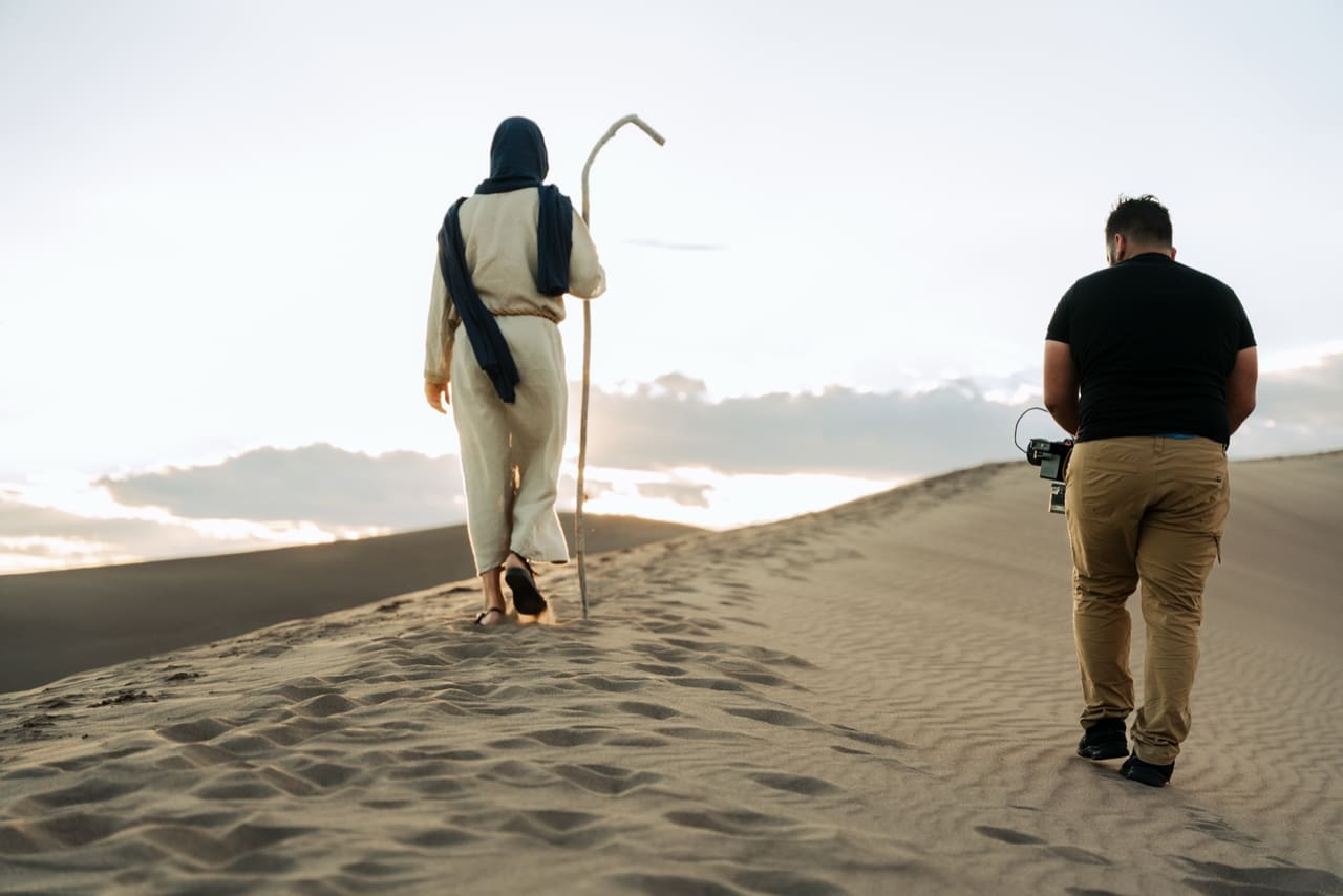 Actor in costume and crew walking across sand dunes