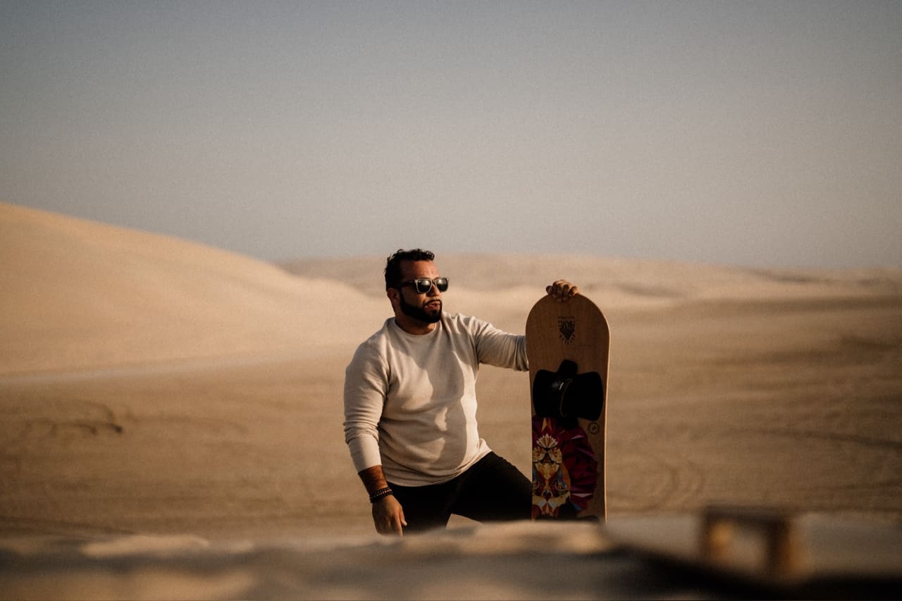 Man kneeling in the desert holding a sandboard